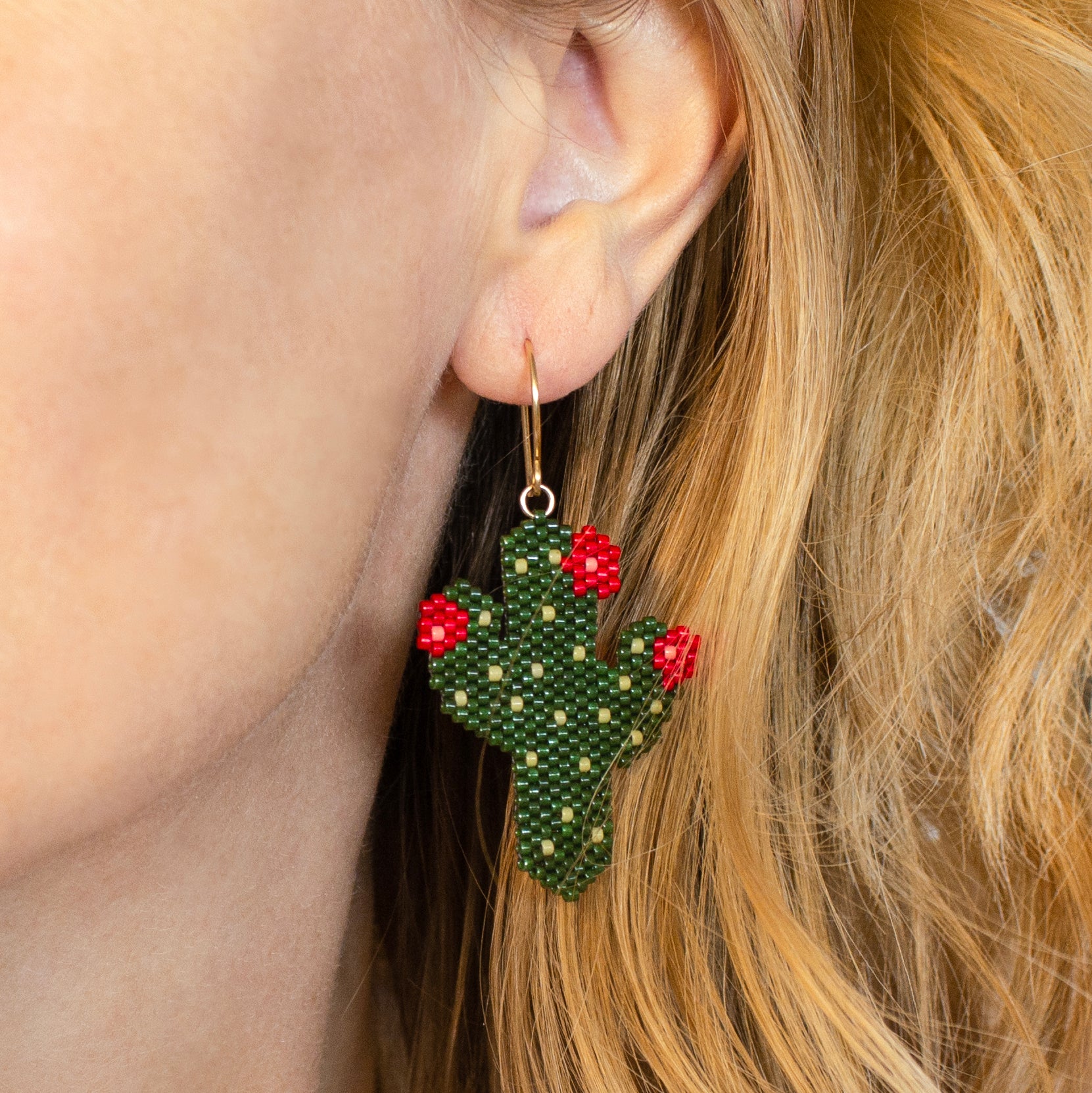 Green beaded cactus earrings with red flowers worn by a person with blonde hair.