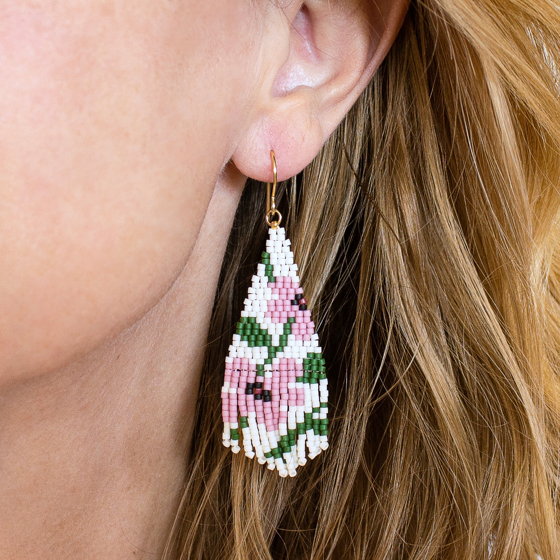 Close-up of a woman wearing a floral beaded earring with pink and green colors.