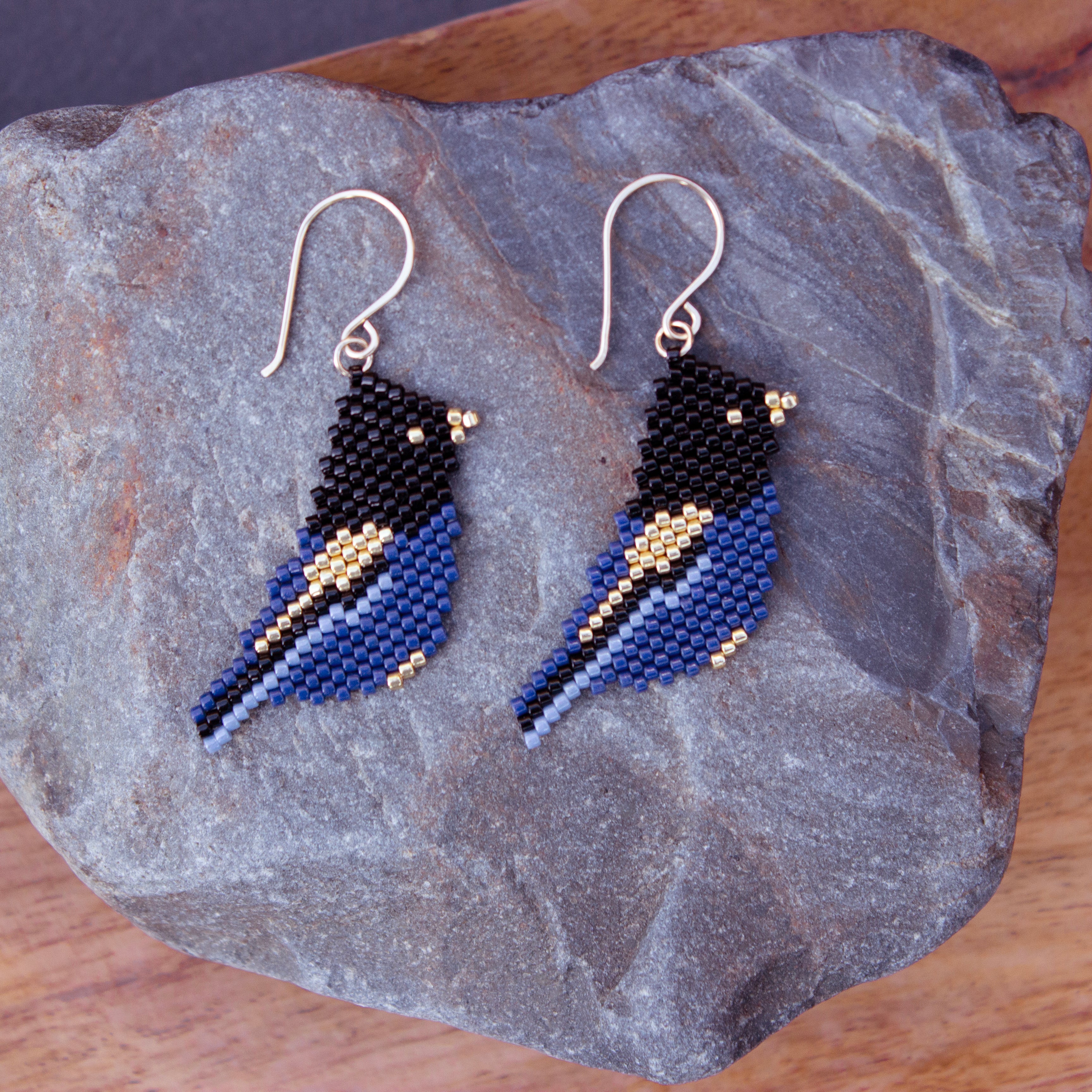 Handcrafted royal blue and black bird dangle earrings displayed on a natural slate stone block