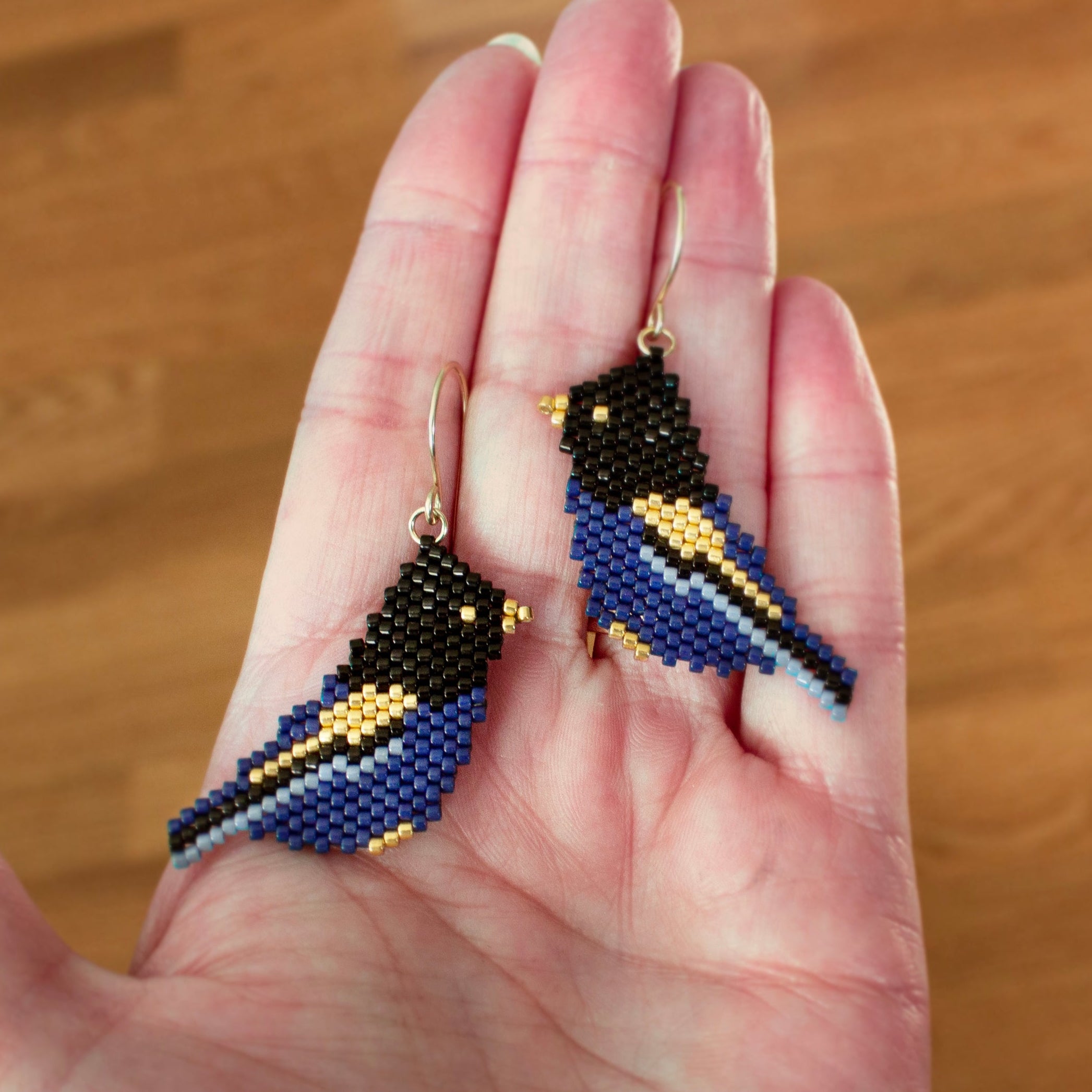 Close up photo showing the scale of the glass beaded Steller's Jay bird earrings being held in a hand